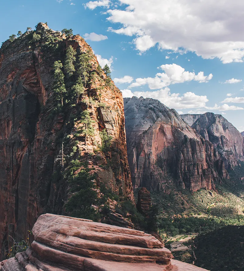 Mountain range in southern Utah. Very steep rocky cliffs with one particular cliff in the foreground with juniper trees growing on it.