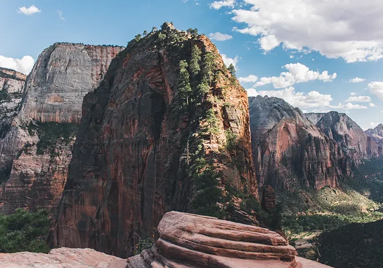 Mountain range in southern Utah. Very steep rocky cliffs with one particular cliff in the foreground with juniper trees growing on it.